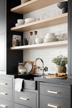 a kitchen with gray cabinets and white subway backsplashes, open shelving above the sink