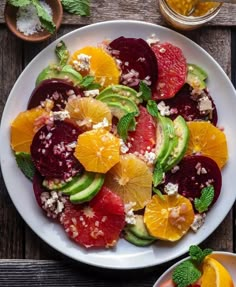 a white plate topped with fruit salad next to another plate filled with oranges, avocado and other fruits