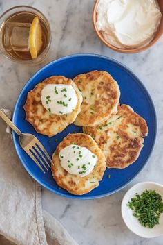 three pancakes on a blue plate topped with sour cream and chives next to a bowl of whipped cream