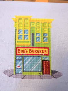 a cross stitch picture of a building with the words ebs burgers on it