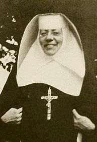 an old black and white photo of a nun with a cross on her chest, standing in front of a tree