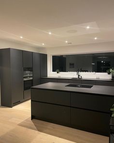 a kitchen with black cabinets and an island in the middle is lit by recessed lights