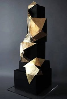 a black and gold sculpture sitting on top of a metal stand in front of a gray wall