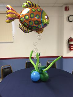 some balloons floating in the air over a table with chairs and a balloon fish on it