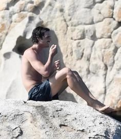 a shirtless man sitting on top of a rock