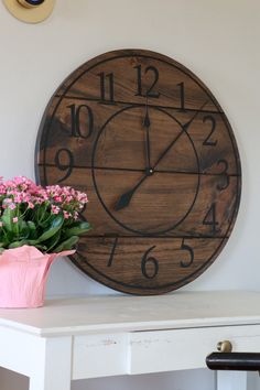 a large wooden clock mounted to the side of a wall next to a potted plant