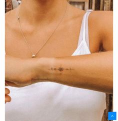 a woman wearing a white tank top holding her arm with a cross tattoo on it