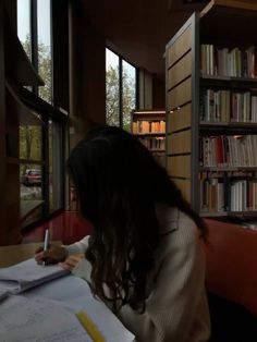 a woman sitting at a table in front of a book shelf filled with books and papers