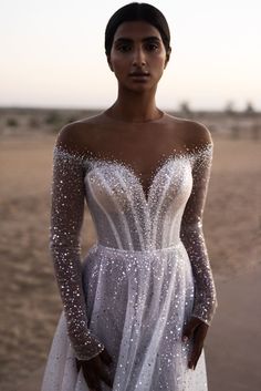 a woman standing in the desert wearing a white dress with sequins on it