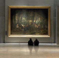 two people sitting on the floor in front of a painting that looks like they are looking at horses