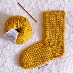 a pair of yellow knitted socks next to a skein of yarn