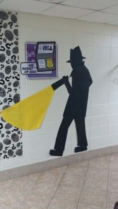 a man with a yellow duster is standing in front of a wall mural that has a silhouette of a man holding a broom