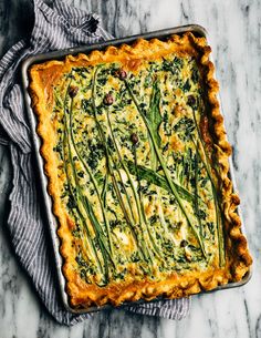 a quiche with asparagus and spinach in a metal pan on a marble surface