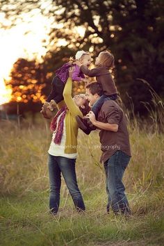 three people are standing in the grass with one holding a baby up to their head