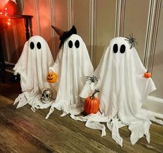 three white ghost statues sitting on top of a wooden floor next to pumpkins and other decorations