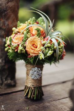 a bridal bouquet with orange roses and greenery on a wooden table in an outdoor setting