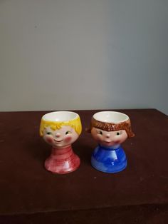 two small cups sitting on top of a brown table next to each other with faces painted on them