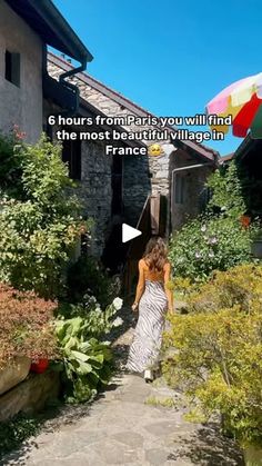 a woman walking down a stone path in front of a house with an umbrella over her head