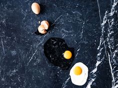 three eggs and one egg on a black marble counter top, with the rest of an egg laying next to it