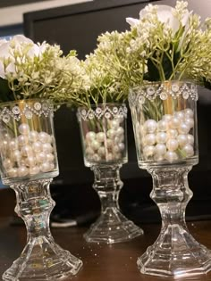 three glass vases with flowers and pearls in them