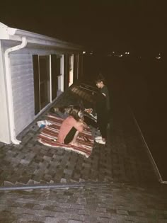 two people standing on the roof of a house at night with one person laying down