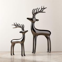 two metal deer sculptures sitting next to each other on a white floor with a wall in the background