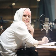 a man with pink hair sitting in front of a microphone and looking at the camera