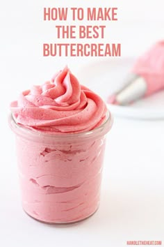 a pink frosted dessert in a glass cup with a spoon next to it on a white surface