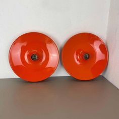 two orange plates sitting next to each other on a shelf in front of a white wall