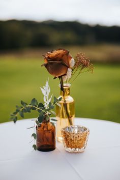 two vases filled with flowers sitting on top of a white table covered in greenery