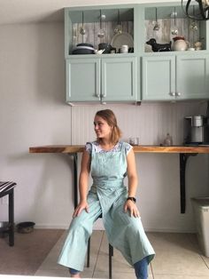 a woman sitting on top of a chair in a kitchen next to a table and cupboards