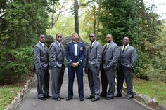 a group of men standing next to each other in front of trees and bushes with one man wearing a suit