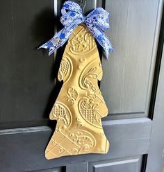 a gold christmas tree shaped cookie hanging on a door with a blue and white bow