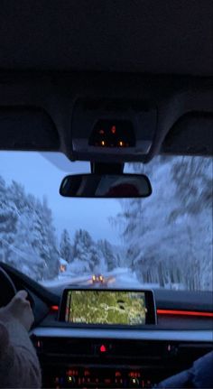 the inside of a car driving down a snow covered road with trees in the background