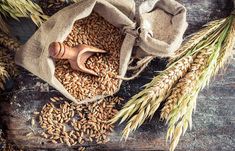 an assortment of grains in a bag on a wooden table next to some ears of wheat