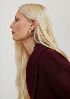 a woman with long blonde hair and earrings looking off to the side, wearing a burgundy top