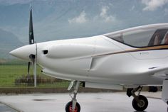 a small white airplane sitting on top of an airport tarmac with mountains in the background