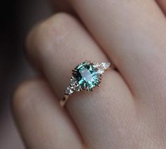 a woman's hand holding a ring with an aqua and white diamond in it