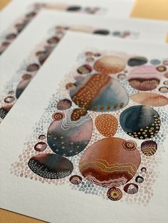 three different colored rocks on white paper with gold and black dots in the middle, sitting on a wooden surface