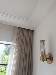 a wall light mounted on the side of a white wall next to a window with drapes