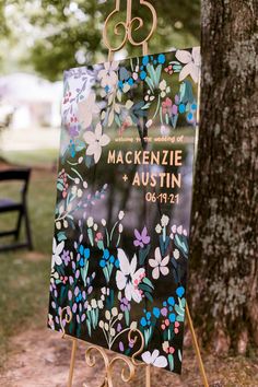 a sign with flowers painted on it in front of a tree