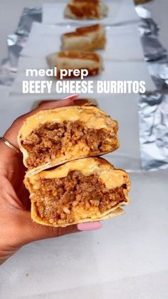 a hand holding up two burritos with meat and cheese on them in front of foil