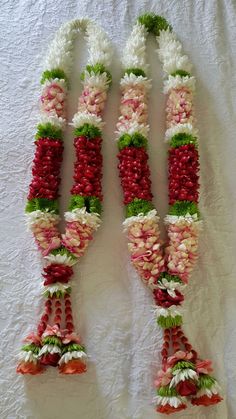 three flower garlands are laid out on a white tablecloth, one is red and the other is green