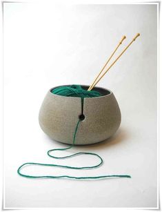 a yarn ball and two knitting needles in a gray bowl with green string on the side