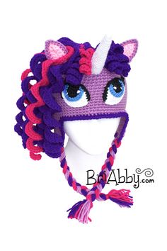 a crocheted unicorn hat with blue eyes and pink manes on the side