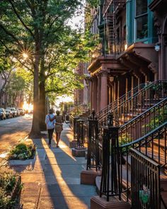 people walking down the sidewalk in front of some buildings with trees on both sides and stairs leading up to them