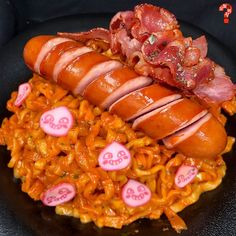 two hotdogs and macaroni on a black plate with heart shaped candies