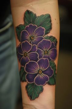 a woman's arm with purple flowers and green leaves on the left side of her arm