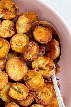 a pink bowl filled with fried potatoes on top of a white tablecloth next to a spoon