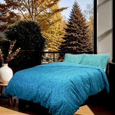 a bed sitting next to a window on top of a wooden floor covered in blue sheets